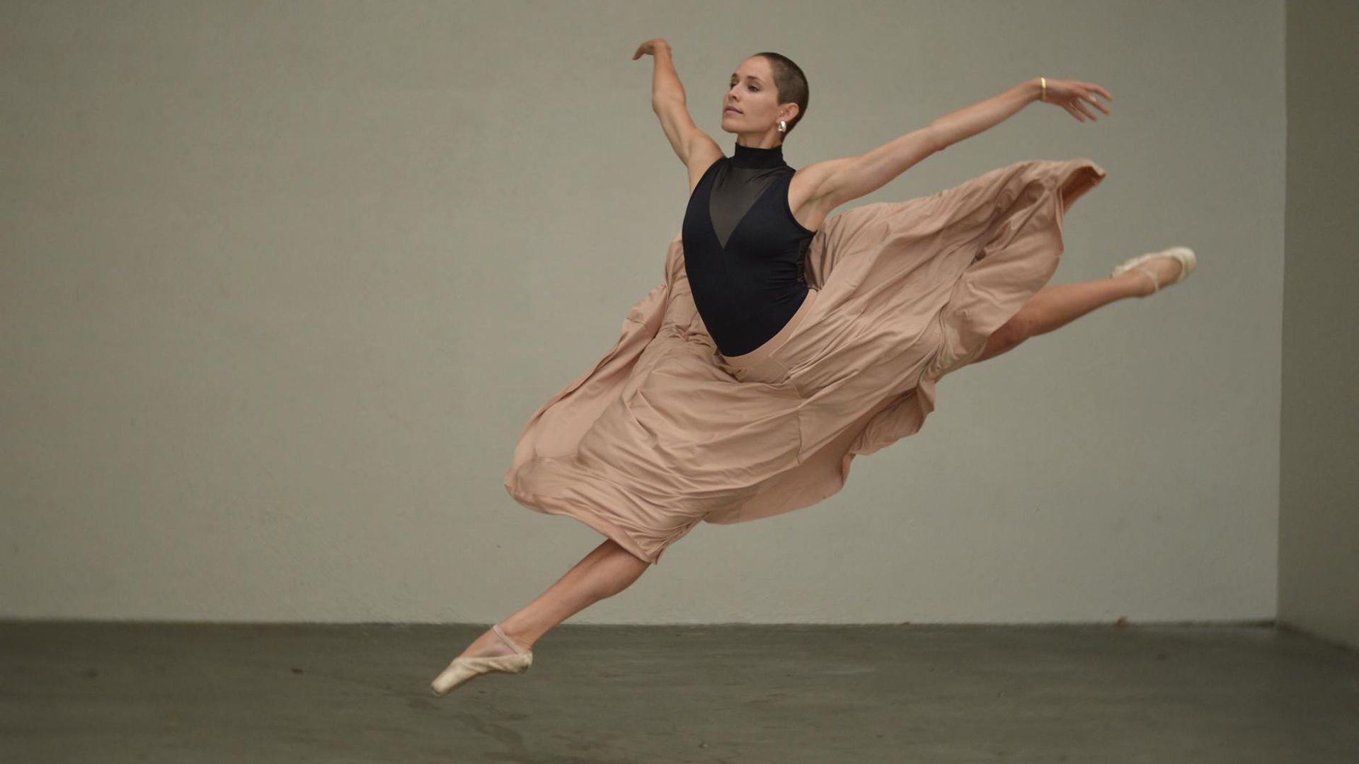 Person performing a dynamic stretching movement in a minimalist dark space.